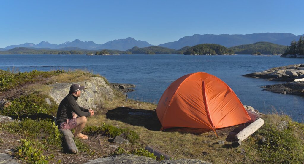 Man sits next to tent, pitched on island in the middle of nowhere.