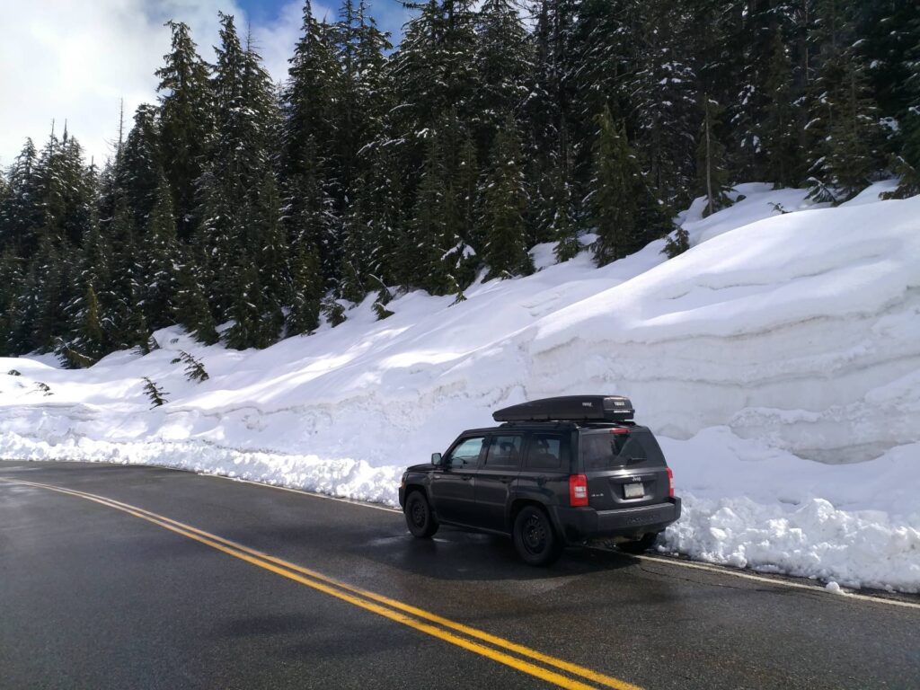 Jeep parked at side of road, with wall of snow taller than the car.
