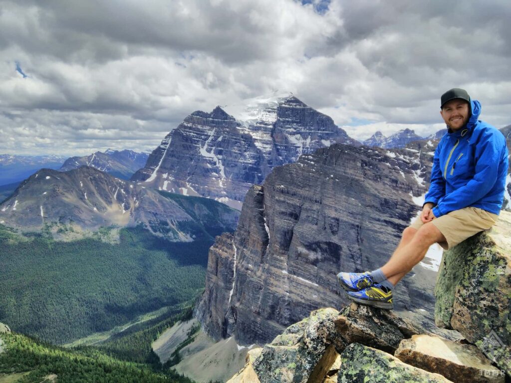 Seb sat at the top of Mount Fairview with the steep peaks of the Rocky Mountains behind