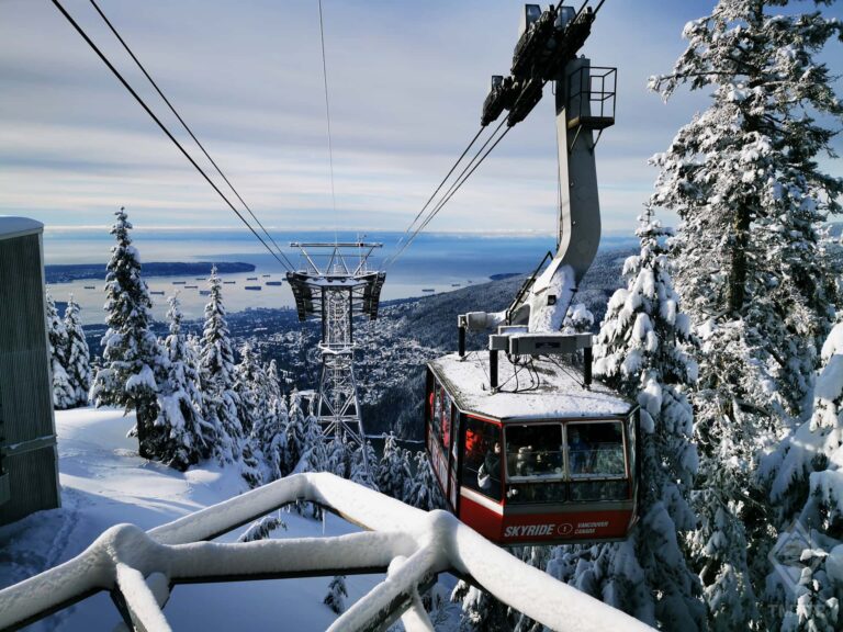 Snow covered mountain gondola with city behind.