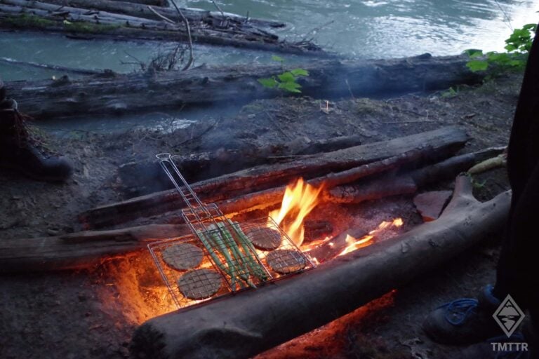 A DIY campfire made of logs, with burgers cooking.
